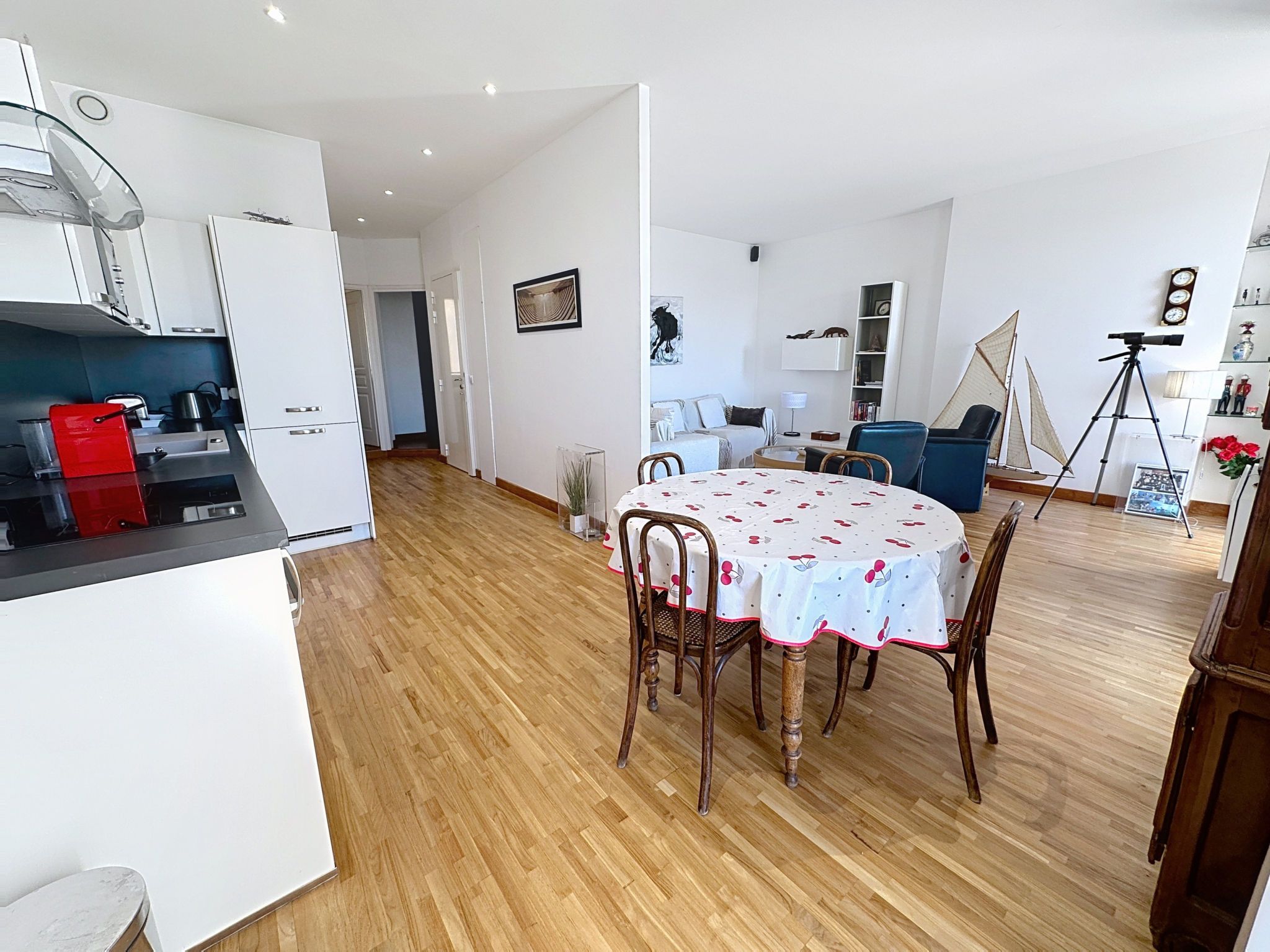 A modern kitchen with white cabinets, a red toaster, and a dining area with a round table and chairs.