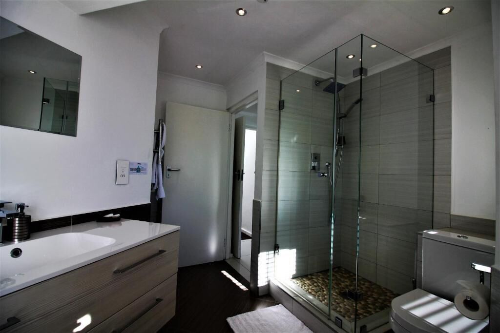 A modern bathroom with a glass-enclosed shower, a white sink, and a toilet.