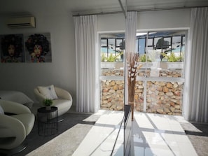 Una sala de estar moderna con un sofá, una mesita auxiliar y un ventanal con una pared de piedra.