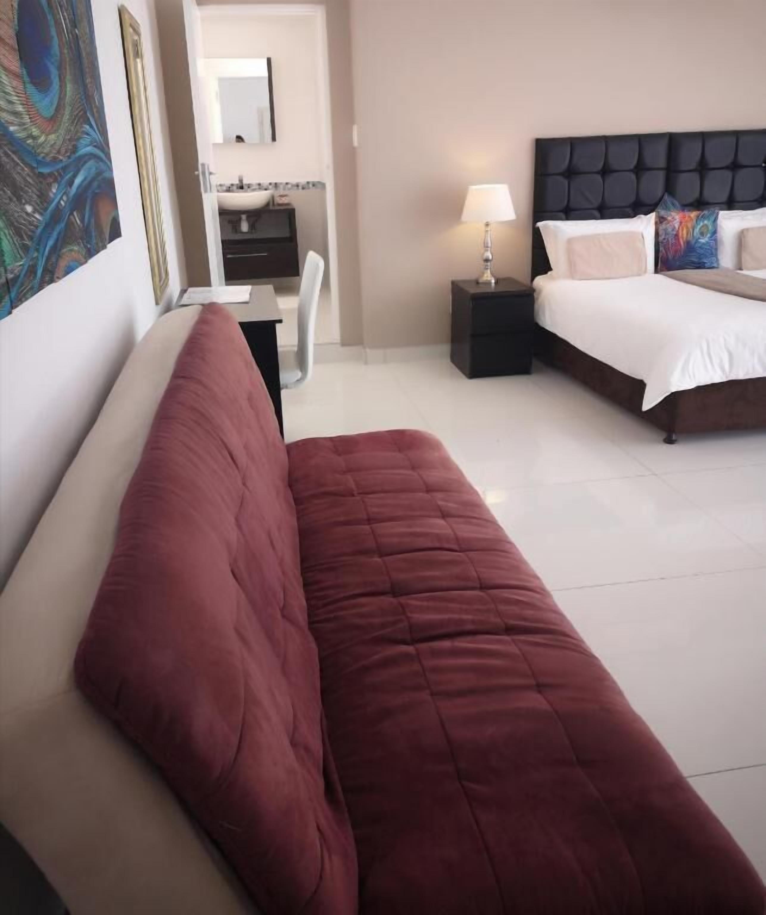Habitación de hotel con cama, mesita de noche con lámpara, una silla y un cuadro en la pared.