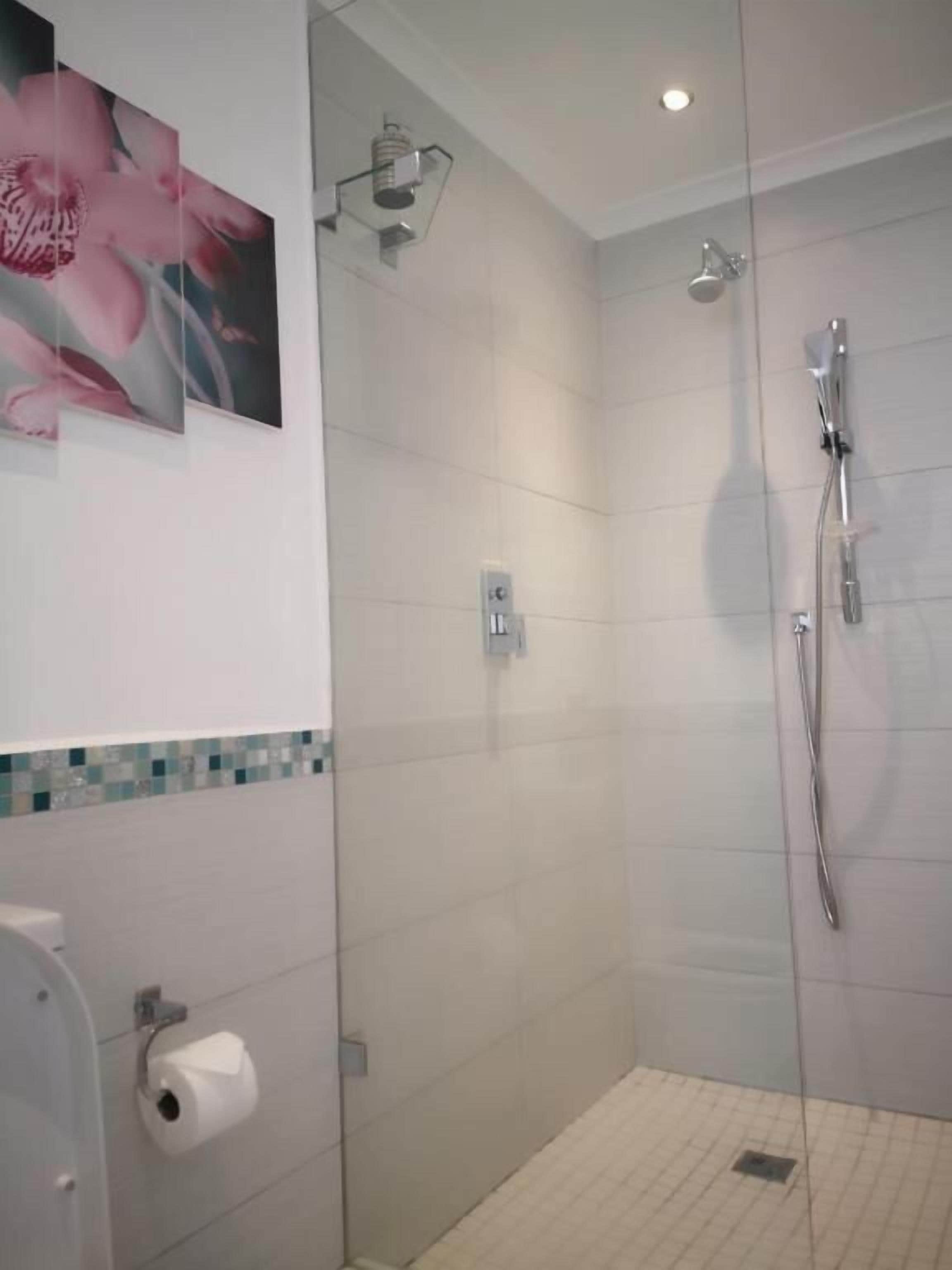 Une douche avec une porte en verre, un sèche-mains et un porte-rouleau de papier toilette.