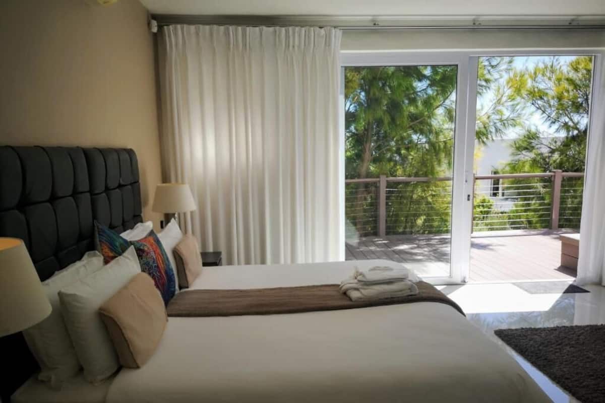 Une chambre d’hôtel avec un lit, une table de chevet, une lampe, une fenêtre avec des rideaux et une vue sur l’extérieur.