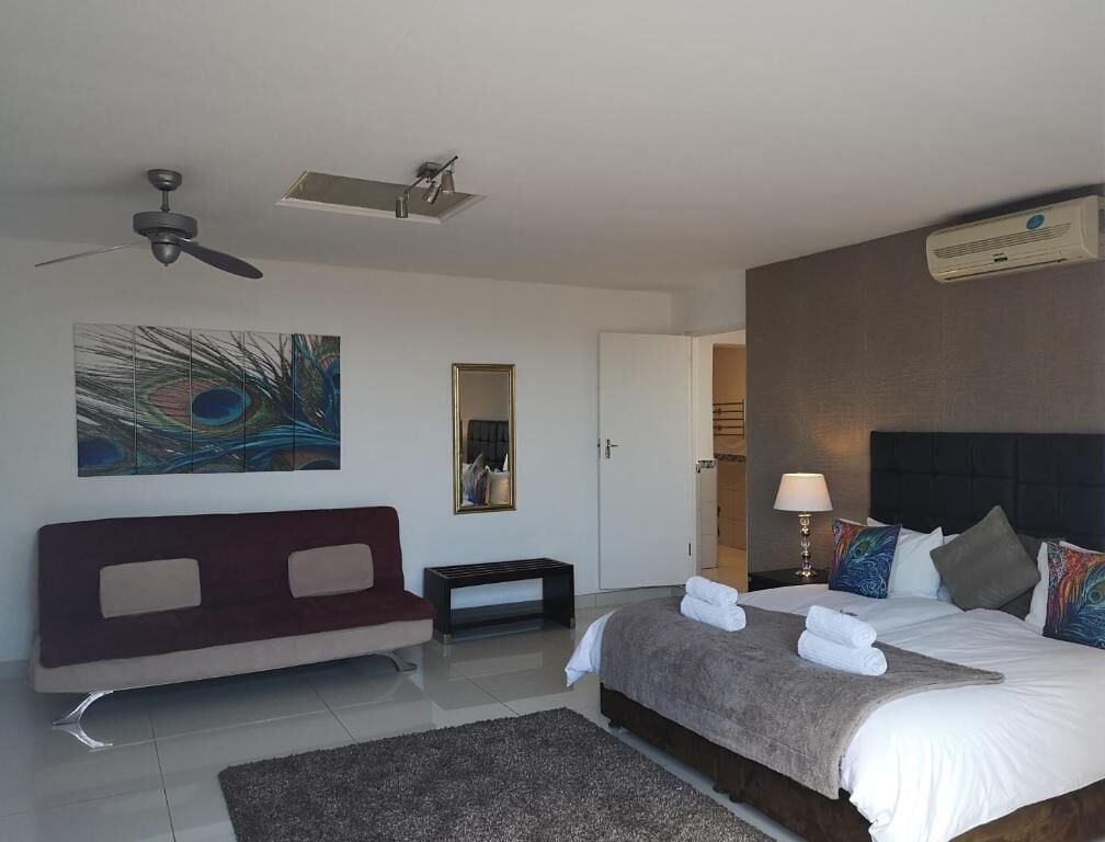 Une chambre d’hôtel avec un lit, un canapé, un ventilateur de plafond, un tableau, un miroir et une porte.