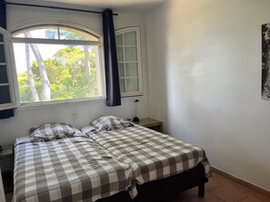 A bedroom with a bed, a window with curtains, a bedside table, and a wall-mounted light fixture. - 90m2 apartment (1st floor) in Port d'Alon, 4 persons, dogs welcome. (Saint-Cyr-sur-Mer)