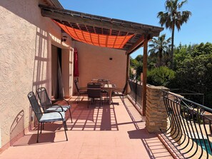 Une terrasse avec une table et des chaises, une pergola en bois et un mur en pierre.
