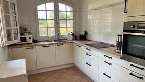 A kitchen with white cabinets, a microwave, a sink, and a window with a view of greenery. - 90m2 apartment (1st floor) in Port d'Alon, 4 persons, dogs welcome. (Saint-Cyr-sur-Mer)