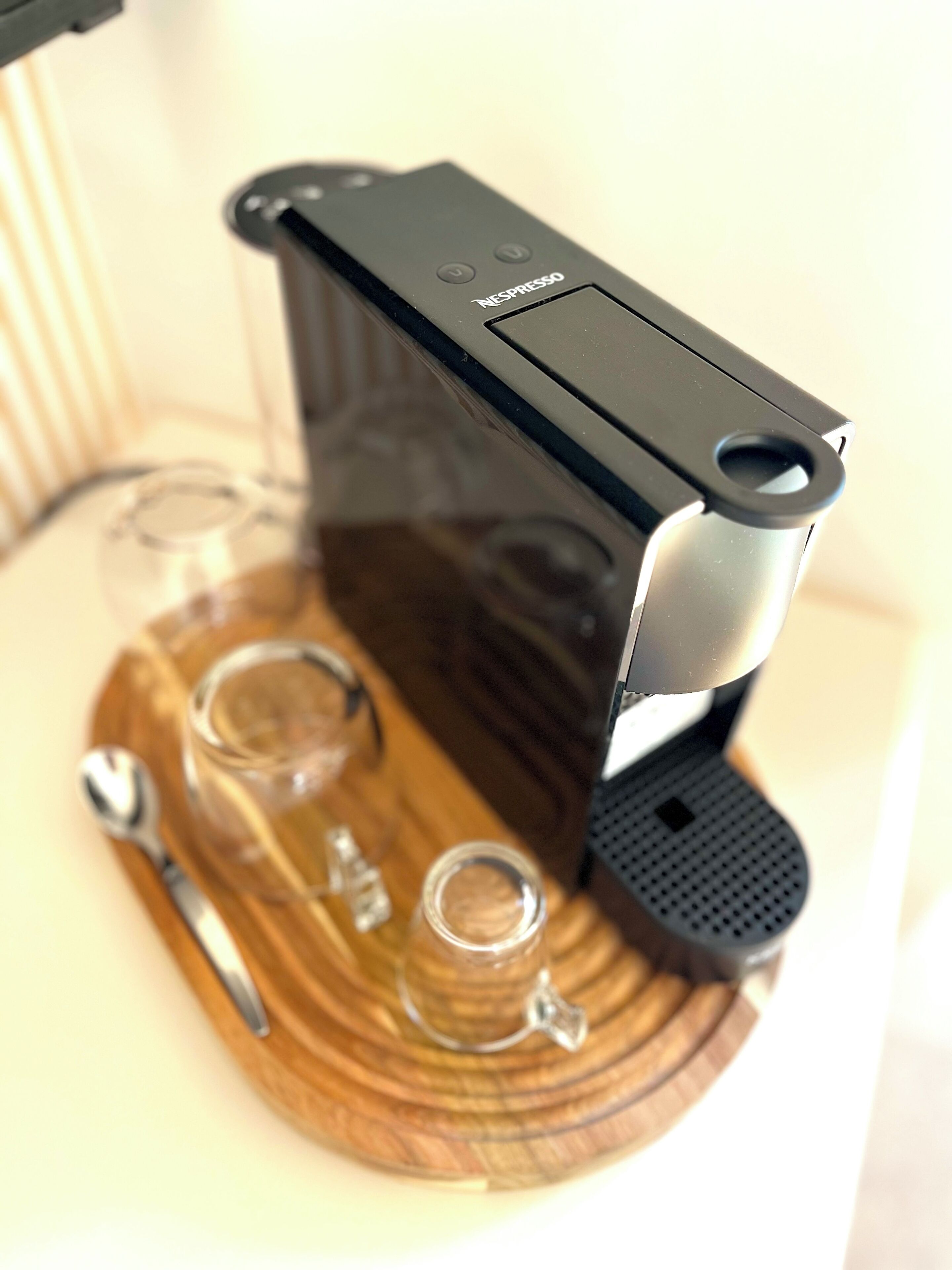 A Nespresso coffee machine on a wooden coaster with a spoon and two glasses.