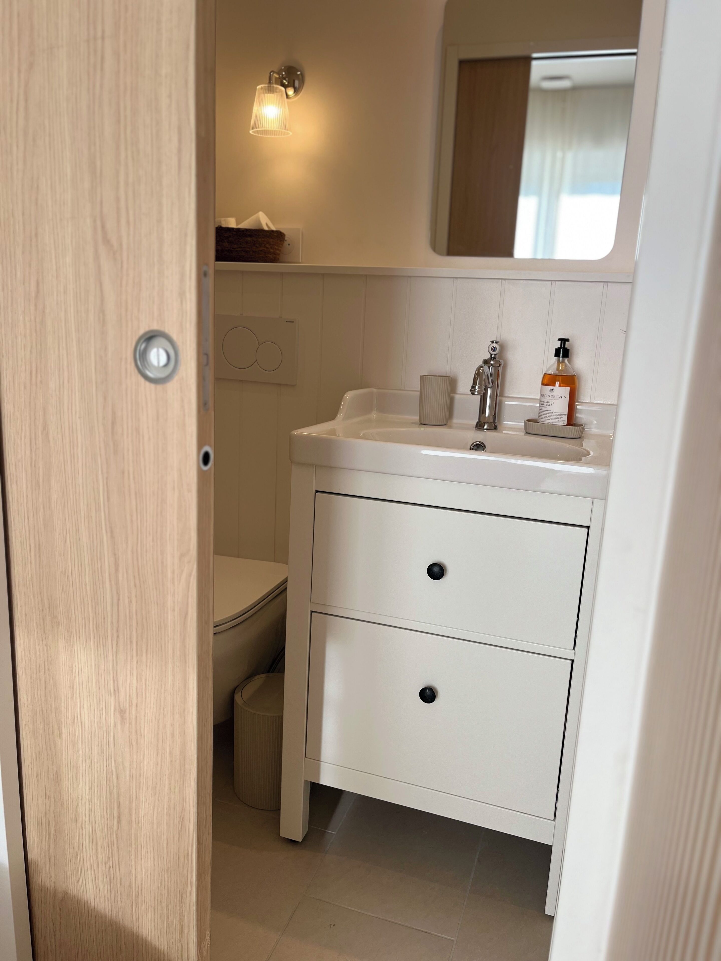 A compact bathroom with a white sink, two drawers, a mirror, and a toilet.