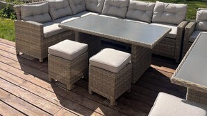 Un área de estar al aire libre con muebles de mimbre, cojines, una mesa y otomanas en una terraza de madera.