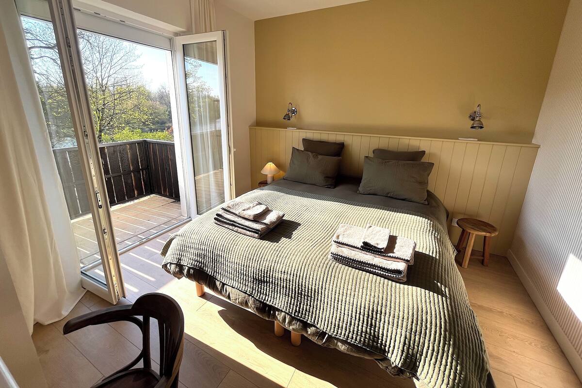 A bedroom with a bed, a nightstand, a lamp, a chair, and a sliding glass door leading to a balcony.