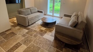Un salón amplio con un sofá, un sillón, una mesa de centro y un televisor fijado a la pared.