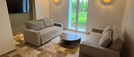 A spacious living area with a sofa, a smaller chair, a coffee table, and a TV mounted on the wall.