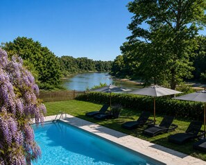 A swimming pool with lounge chairs and umbrellas, surrounded by greenery and a river view. - Le Clos des Berges de l'Ain (Charnoz-sur-Ain)