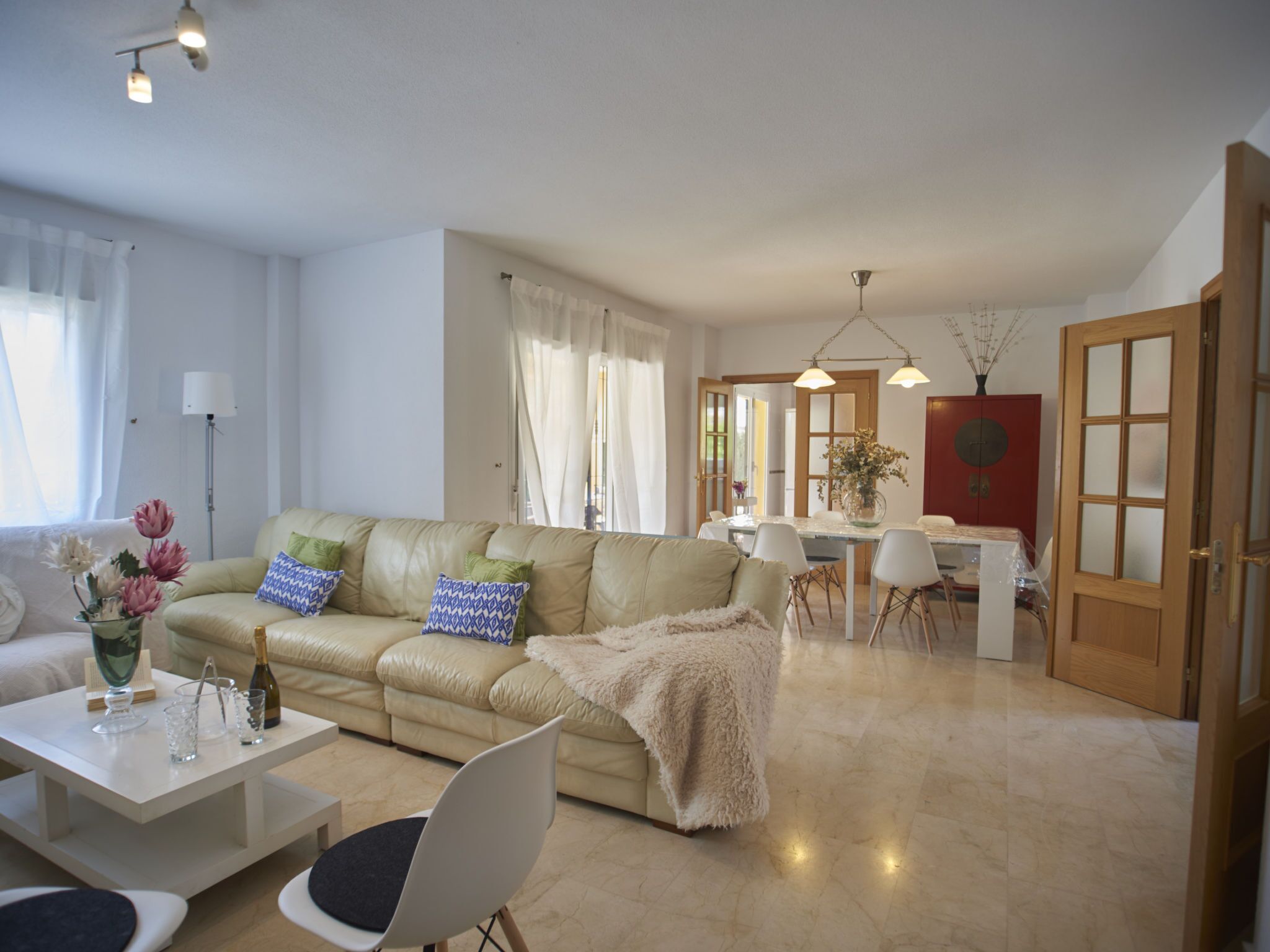 Una sala de estar moderna con un sofá color beige, una mesa de comedor con sillas y una cocina visible a través de una puerta abierta.