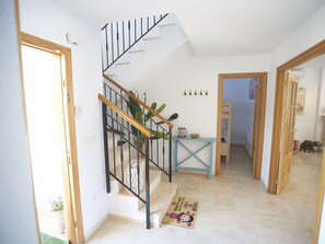 A staircase with a wooden handrail and black balusters, leading to a landing with a blue table and a decorative mat. - VILLA 25 by Interhome (Mutxamel)