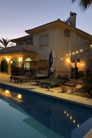 A poolside area with lounge chairs and umbrellas, a clear pool, and string lights. - VILLA 25 by Interhome (Mutxamel)