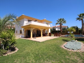 Ein zweigeschossiges Haus mit Terrasse, umgeben von einem gepflegten Rasen und Palmen.