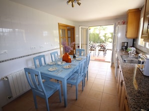 A dining area with a blue table and chairs, a vase with flowers, and a view of the garden through the door. - VILLA 25 by Interhome (Mutxamel)