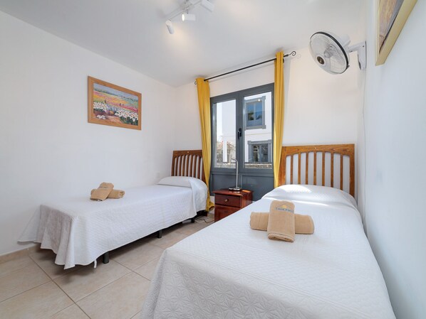 Een hotelkamer met twee eenpersoonsbedden, een nachtkastje, een ventilator aan de muur, een raam met gordijnen en een schilderij.