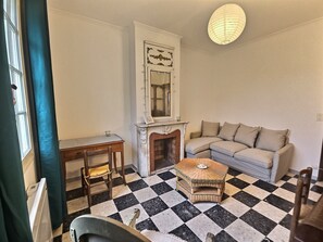 A living room with a checkered floor, a sofa, a small table, a chair, a fireplace, and a hanging light fixture. - Jean House (La Tour D'Aigues)