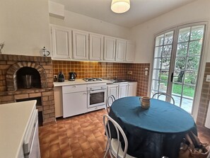 A kitchen with white cabinets, a brick oven, a gas stove, and a dining table with chairs. - Jean House (La Tour D'Aigues)