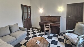 Olohuoneessa on ruutukuviollinen lattia, sohva, nojatuoli, piano ja lamppu.