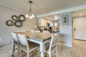 A dining area with a wooden table and white chairs, a kitchen in the background, and a white door. - Walk to St Augustine Beach! Resort-Style Condo (St. Augustine)