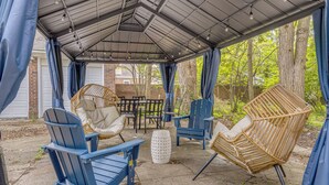 Un espacio de patio cubierto con mobiliario exterior, incluyendo sillas Adirondack azules y una silla de mimbre, además de una mesa.