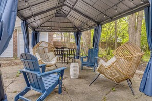 A covered patio area with outdoor seating, including blue Adirondack chairs and a wicker chair, and a table.