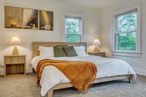A bedroom with a bed, two bedside tables, a window, and a painting on the wall.