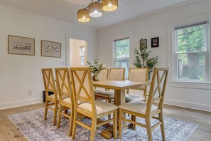 A dining area with a wooden table and chairs, framed artwork on the walls, and large windows.