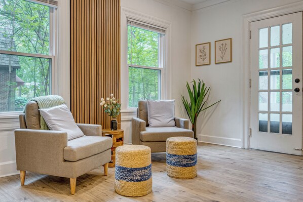 A room with two sofas, a wooden floor, a door with glass panels, and a window with a view of trees.