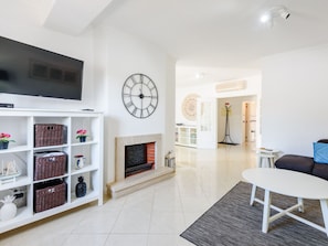 A modern living room with a flat-screen TV, a fireplace, a clock, and a dining area. - Apartment  by Interhome (Albufeira)