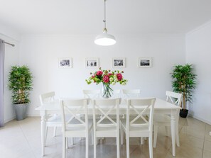 Un coin repas avec une table et des chaises blanches, un luminaire suspendu et des tableaux encadrés au mur.