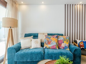 Un salon moderne avec un canapé bleu, des coussins décoratifs, une lampe sur pied et un mur à rayures.