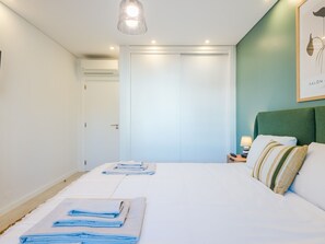 Une chambre d’hôtel avec un lit, une table de chevet, une lampe, un tableau encadré au mur et une porte.