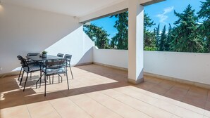 Ein geräumiger Balkon mit Tisch und Stühlen, freier Blick auf Bäume und eine weiße Wand.