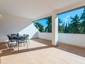 A spacious balcony with a table and chairs, a clear view of trees, and a white wall. - Apartment  by Interhome (Albufeira)