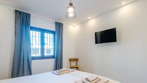 Ein Hotelzimmer mit einem Bett, einem Sessel, einem an der Wand befestigten Fernseher und einem Fenster mit Vorhängen.