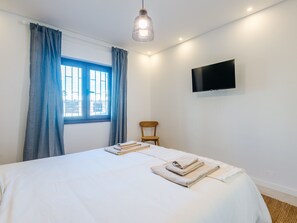 A hotel room with a bed, a chair, a TV mounted on the wall, and a window with curtains. - Apartment  by Interhome (Albufeira)
