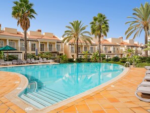 Ein Swimmingpool mit Liegestühlen und Palmen, umgeben von einem Gebäude mit einem Ziegeldach.