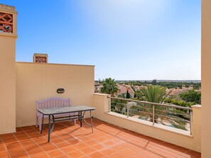 A balcony with a table and a bench, overlooking a residential area with palm trees and houses. - Apartment  by Interhome (Quarteira)