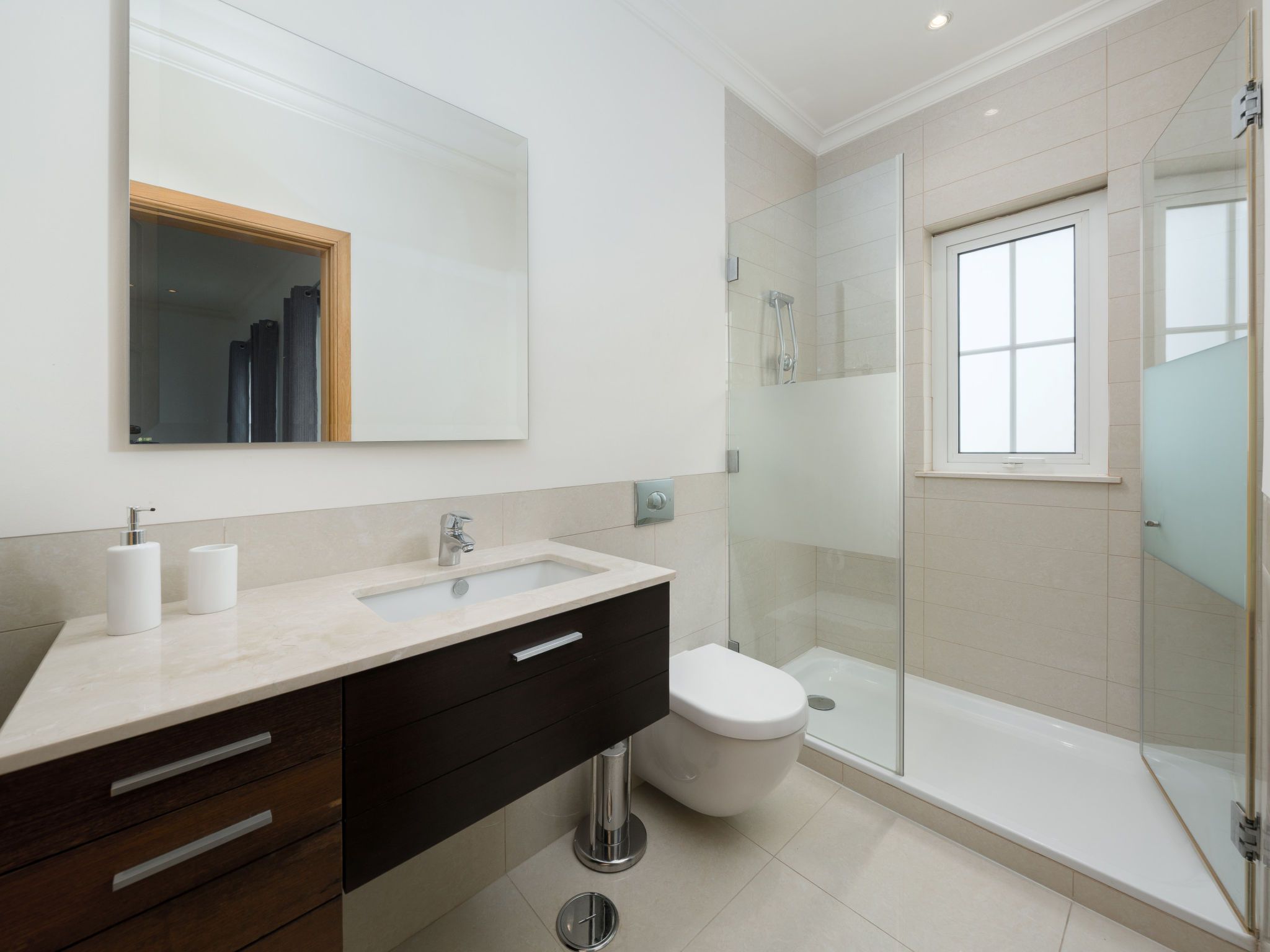 Un baño moderno con un espejo grande, un lavabo, un inodoro y una ducha con mampara de vidrio.