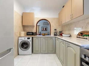 A compact kitchen with a washing machine, a sink, and a fruit bowl on the counter. - CARVOEIRO POOL HOUSE by VACATIONY by Interhome (Carvoeiro (Algarve))
