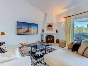 A modern living room with a fireplace, a flat-screen TV mounted on the wall, and a large window with curtains. - CARVOEIRO POOL HOUSE by VACATIONY by Interhome (Carvoeiro (Algarve))