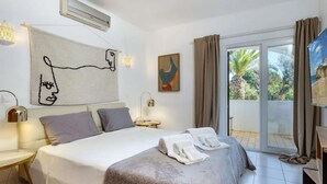 A hotel room with a bed, a painting, a window with curtains, and a view of the outdoors. - CARVOEIRO POOL HOUSE by VACATIONY by Interhome (Carvoeiro (Algarve))