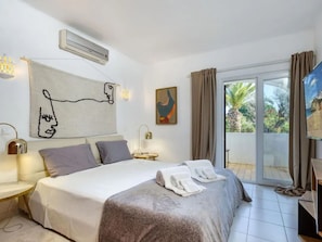 A hotel room with a bed, a painting, a window with curtains, and a view of the outdoors. - CARVOEIRO POOL HOUSE by VACATIONY by Interhome (Carvoeiro (Algarve))