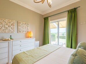 A bedroom with a bed, a dresser, a lamp, and a view of the outdoors through a sliding door. - Apartment  by Interhome (Lagos)