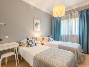 A hotel room with two beds, a desk, a chair, a lamp, and a large window with curtains. - Boavista Charming Apartment by Interhome (Lagos)