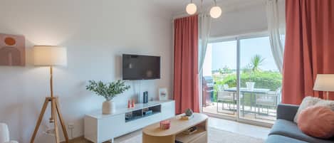 Una sala de estar moderna con una televisión de pantalla plana, una mesa de centro de madera, un sofá y un ventanal con cortinas.